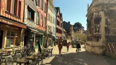 Fransa 'nın Rouen şehrinde 3 Nisan 2025' te yarı keresteli binalarla renkli bir cadde boyunca yürüyen insanlar heykellerle dolu tarihi bir taş cephesinin hemen yanındalar. 
