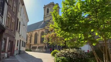 İnsanlar 28 Mart 2025 'te Rouen France' da çiçek açan ağaçlar ve sabah güneşiyle gotik bir kiliseye doğru yürüyorlar. 