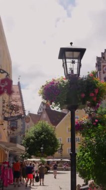 24 Temmuz 2025 'te tarihi Fuessen kasabasında yürüyen insanlar geleneksel binalar ve canlı yaz çiçekleriyle aydınlık gün ışığında 