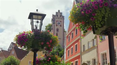 Renkli çiçeklerle süslenmiş eski bir sokak feneri ve güneşli bir yaz gününde Fuessen Almanya 'nın arka planında tarihi bir şehir kulesi 