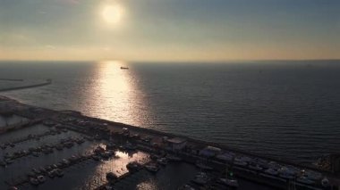 Limandaki panoramik hava manzarası ve eğimli dalgakıranlar liman boyunca yanaşan kayıkları ve pürüzsüz su yüzeyini gösteriyor. 