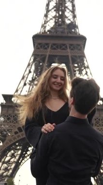 Güneşli bir günde Paris 'teki Eyfel Kulesi' nin altında gülümseyen ve kucaklaşan mutlu romantik çift.