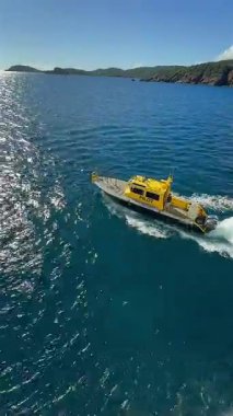 Parlak sarı pilot botu, berrak tropikal sularda yüksek hızda süzülen dalgalar ve mavi gökyüzüyle ilerliyor. 