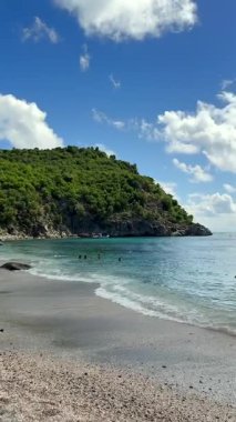 29 Temmuz 2025 'te Karayip Denizi' nde yemyeşil bir uçurumun kenarında okyanusun tadını çıkaran yüzücülerle güneşli tropikal plajlar.