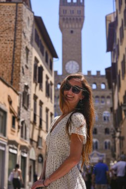Floransa, İtalya 'da güneşli bir sokakta gülümseyen benekli elbiseli genç bir kadın. Arka planda Palazzo Vecchio var. Mükemmel seyahat ve yaşam tarzı anı 