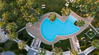 Palmiye ağaçları, şezlonglar ve tropikal lüks bir tatil beldesindeki bahçe yollarıyla çevrili kalp şeklinde bir yüzme havuzu.