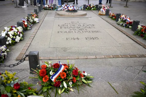 Taze kırmızı ve beyaz çiçekler yeşil yapraklar ve üç renkli kurdelelerle bir bukete yerleştirilmiş gün ışığında taştan bir yüzeye yerleştirilmiş.