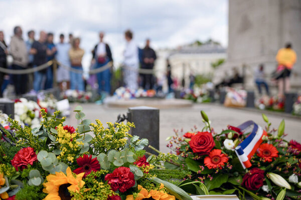 Bouquet with red white and yellow flowers placed at a memorial site in Paris during a ceremony with people blurred in the background