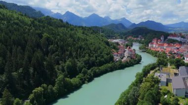 Fussen, Almanya 'nın insansız hava aracı videosu, Lech Nehri, tarihi kasaba binaları ve açık gün ışığında manzaralı dağlık alan. 
