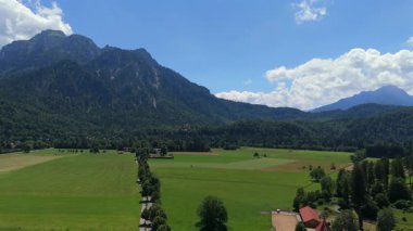 Güney Almanya 'da Fussen yakınlarında yeşil yaz çayırları ve sık dağlık alan manzaralı dağ manzaralı bir hava videosu. 