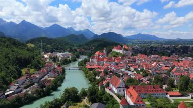 Almanya 'nın Fussen kentinin panoramik hava görüntülerinde tarihi bir tepe şatosu, Lech Nehri ve manzaralı dağ manzarası yer alıyor. 