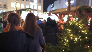 14 Aralık 2024 'te Münih' teki Noel pazarında aydınlatılmış bir Noel ağacının yanında duran küçük bir Noel Baba şapkası takan kadın. 