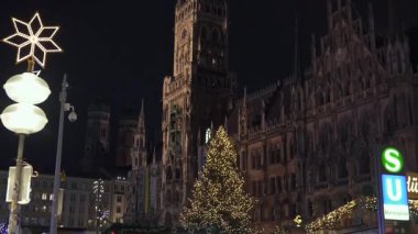 Münih Marienplatz 'ın 14 Aralık 2024' te yeni belediye binasının Noel ışıkları ve şenlikli dekorasyonlarını gösteren gece görüntüsü 