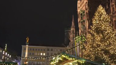 14 Aralık 2024 'te Münih' te Marienplatz, Almanya 'da yeni belediye binası ve Mariensaule' de süslenmiş pazar tezgahlarıyla aydınlatılmış Noel ağacı 