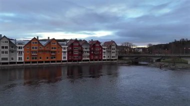 Steinkjer Norveç 'te nehir kenarındaki renkli evlerin manzarası. Köprüsü ve bulutlu akşam gökyüzü altında sakin bir su. 