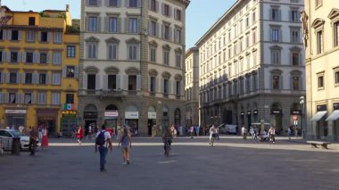 İnsanlar 4 Temmuz 2025 'te Floransa İtalya' da tarihi binalar ve dükkanlarla güneşli meydanda bisiklete biniyor ve yürüyor. Sadece editör kullanımı