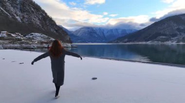 Turist kadın, karlı dağlarda kışın fiyort manzarasının tadını çıkarıyor.