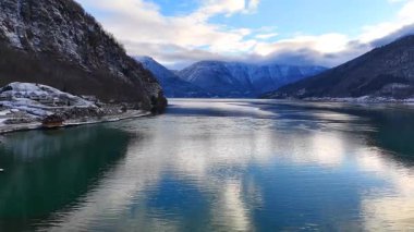 Norveç 'in Gaupne kentindeki fiyort, sakin turkuaz sularla bulutları, karla kaplı dağ yamaçlarını ve sakin doğal manzarayı yansıtıyor..