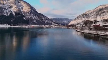 Norveç 'in Gaupne şehrinde kışın fiyort manzarası turkuaz sular, karlı dağlar ve küçük liman