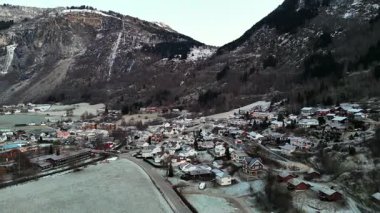 Norveç 'in Gaupne bölgesindeki karlı tarlalar ve kümelenmiş evler kış ışığı ve dik dağ kayalıkları altında 