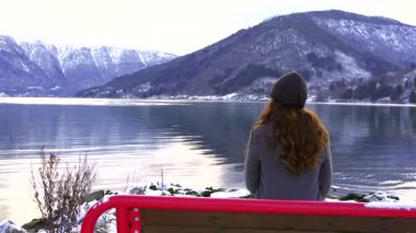 Kürsüde oturan kadın sakin kış fiyortlarına ve dağ manzarasına bakıyor.