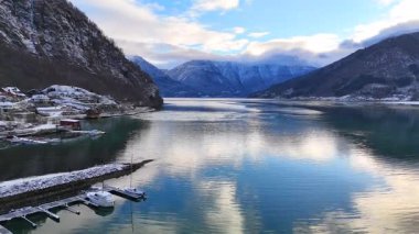 Yansımaları olan sakin fiyort, kıyı boyunca karlı tepeler ve evler.
