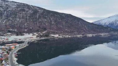 Karla kaplı dağlar, durgun fiyortlu sularda yansıyor. Kış manzaralı.