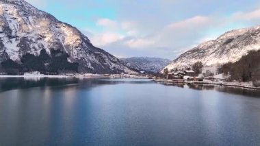Buzlu mavi suyu, karlı kıyı şeridi ve kışlık evleri olan fiyordun yakın görüntüsü.