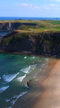 Sahilde kayalıklar yumuşak dalgalar yeşil tarlalar ve kıyıda büyük kayalar 