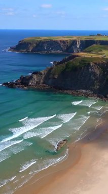 Dalgaları büyük kaya sarp kayalıkları ve mavi gökyüzü manzarası olan sahil. 