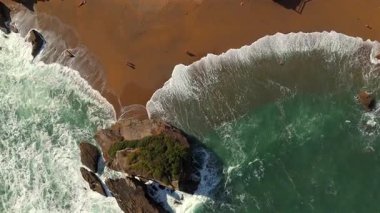 Dalgalar kumlu sahile ulaşıyor ve insanlar yürüyor. 