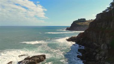 Dalgalı kayalıklar ve uzak kumlu bir sahil 