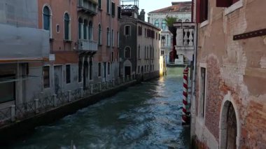 Çizgili gondol direkleri ve tarihi binaları olan kanal Venedik