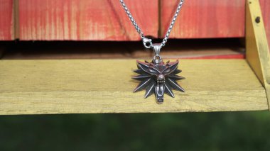 A close-up of a metal wolf-shaped , witcher-inspired pendant on a wooden background.  clipart