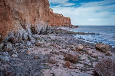 Ardrossans plajının manzaralı kıyı manzarası. Büyük kayalar ve deniz yosunları kumlu sahili kirletir. Suya uzanan ahşap ahşap oyuklar vardır..