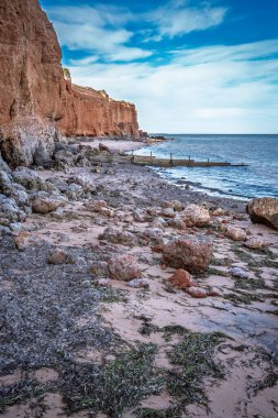 Ardrossans plajının manzaralı kıyı manzarası. Büyük kayalar ve deniz yosunları kumlu sahili kirletir. Suya uzanan ahşap ahşap oyuklar vardır..