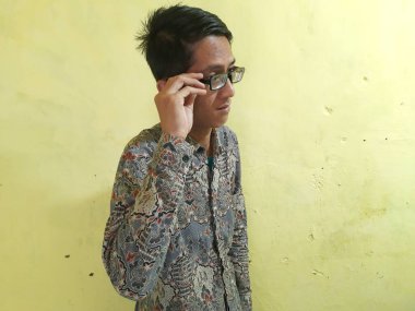 Takım elbiseli ve gözlüklü bir adam telefonla konuşuyor, kameraya bakıyor.