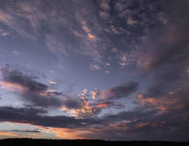 Soluk kesici bir günbatımı gökyüzü dramatik pastel renkli bulutlarla boyanmış, sıcak ve serin tonlarını sakin ama dinamik bir kompozisyonda harmanlıyor..