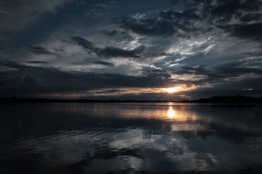 Batan güneşin altın ışınları dramatik bulutları delip geçer sakin göl yüzeyine büyüleyici bir yansıma bırakır. Huysuz ama huzurlu bir manzara, doğa ve güzel sanat fotoğrafçılığı için mükemmel.