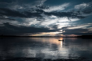 A lone boat floats on a tranquil lake, silhouetted against a moody sky with golden sunset reflections on the water. The vast horizon and cloud formations create an atmospheric and cinematic scene. clipart