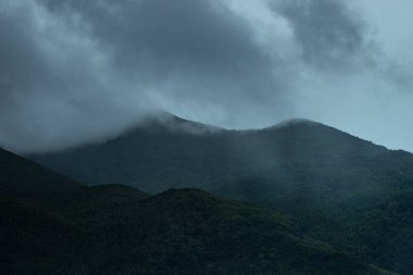 Mauritius 'taki orman kaplı dağ tepelerinin karamsar ve atmosferik bir görüntüsü, kısmen alçak sis ve bulutlarla kaplı..