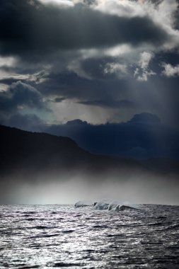 Şiddetli bir deniz manzarası dalgalı bir denizin üzerinde dramatik fırtına bulutları ön planda dalgaların ve arka planda siluetlerin olduğu