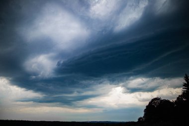 Uğursuz, çok katmanlı fırtına bulutları orman ufkuna yavaşça yaklaşırken gökyüzüne hükmediyor. Aydınlatılmış alçak gökyüzü ve derinleşen üst atmosfer arasındaki gerilim yaklaşan bir fırtınanın dinamik doğasını yakalar..