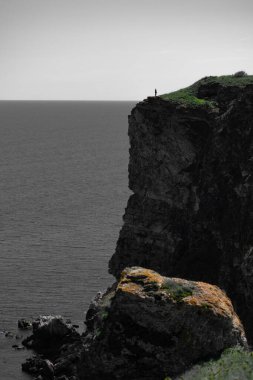 Yalnız bir insan figürü engebeli bir uçurumun kenarında solgun bir gökyüzünün altında engin ve sessiz bir denize bakıyor. Karanlık tonlar ve çimenlerin ve kayaların üzerindeki seçici ışık yalnızlık, saygı ve tefekkür hislerini çağrıştıran güçlü bir kontrastlık yaratır..