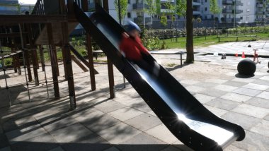 Hareket halindeki bir çocuk, modern bir oyun parkında parlak bir metal kaydırağın üzerinde kayarken yakalandı. Bulanık figür hareketi ve çocukluk aktivitelerinin neşesini vurguluyor