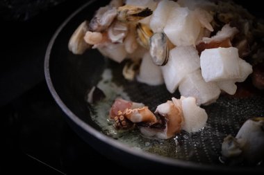 Çeşitli taze ve donmuş deniz ürünleri kızartma tavasında yağda kızartılır. Fotoğrafta yemek pişirme sürecini görüyoruz. Deniz ürünleri az önce ısıtılmış bir tavaya kondu. Lezzetli ve lezzetli görüyoruz.