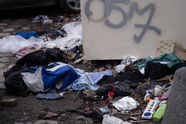 Çöpe atılmış giysiler, çantalar ve çöp tenekesinin yanında grafiti yapılmış bir çöp kutusu. Kentsel atık, geri dönüşüm, kirlilik ve çevre bilinci, şehir hayatı gibi konular için kullanışlı