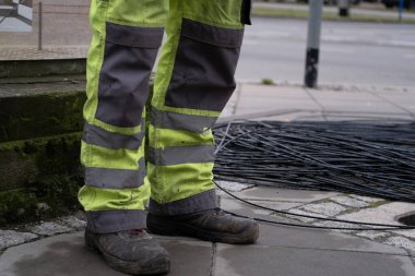 Yansıtıcı bantlı yüksek görüş mesafesi olan bir inşaat işçisinin pantolonu ve botlarının detaylı bir fotoğrafı. İş güvenliği, inşaat alanları, altyapı ve iş güvenliği ile ilgili içerik için ideal