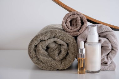 Üç rulo havlu, bej ve kahverengi tonlarda. Yanında da bir şişe damlatıcı ve bir de krema pompası var. Tahta fırça, doğal elementler ve cilt bakımını destekler.