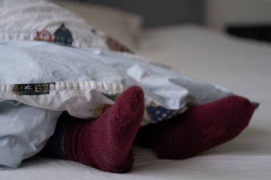 Yumuşak, desenli bir yorganın altından süzülen, kaprisli bir ev baskısı olan sıcak, kahverengi çorapları kapatın. Görüntü sıcaklığı ve konforu yansıtıyor. Kış temaları için mükemmel. Kullanım için ideal.